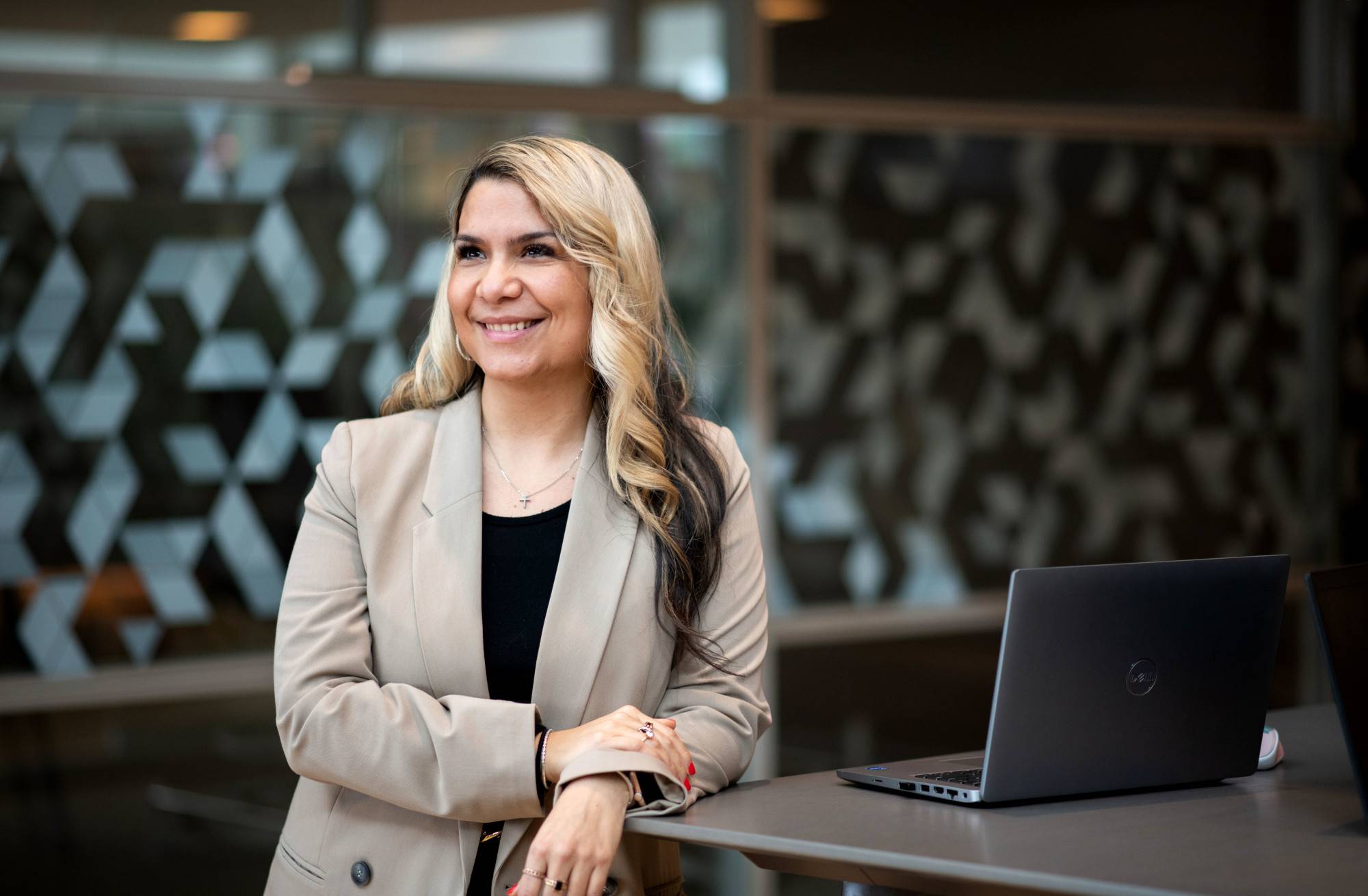 A woman stands looking off into the distance smiling next to a laptop